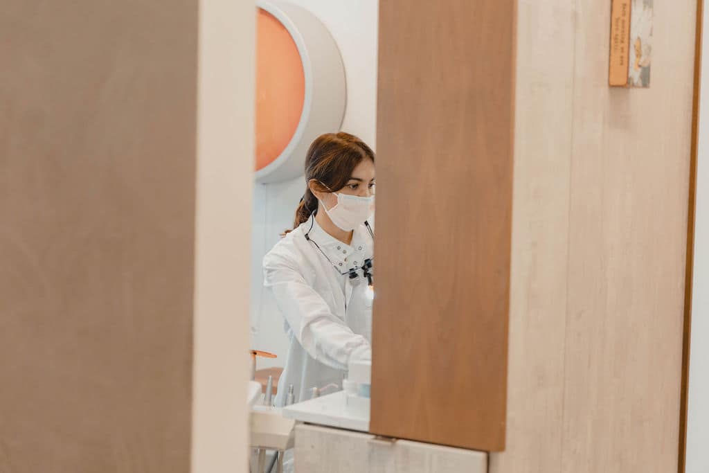 A clinician in loupes, focused mid-treatment, framed through warm wood